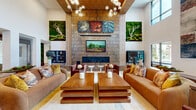 Located at 3421 N Freeway Blvd in Sacramento, CA, this expansive single-floor clubhouse offers a generously sized communal space designed with a sophisticated, nature-inspired aesthetic. The open-plan layout is anchored by a dramatic double-height great room with soaring ceilings clad in warm wood panels and an eye-catching sputnik chandelier arrangement that draws the eye upward. Large clerestory and floor-to-ceiling windows flood the interior with abundant natural light while framing views of the surrounding outdoor community.

A striking textured stone fireplace wall serves as the focal centerpiece of the main lounge, flanked by curated botanical art installations and lush living moss walls that introduce a vibrant organic element throughout. Plush seating areas furnished with rich cognac leather and deep burgundy velvet pieces invite comfortable gathering and relaxation.

A dedicated café-style bar area features a white quartz counter, gold-accented bar stools, and a gleaming gold geometric tile accent wall, complemented by a built-in coffee station and indoor trees. Lighter secondary lounge areas with wood slat partitions, barn-style doors, and large windows provide more intimate spaces for quiet use. Light hardwood-style flooring flows seamlessly throughout, unifying the entire space with a warm, contemporary feel.