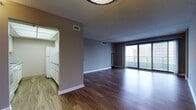 This one-bedroom, one-bathroom unit is thoughtfully laid out across a single floor, offering a well-proportioned living experience with notable urban views. The open living area features warm hardwood-style flooring and neutral gray walls, creating a versatile backdrop for any décor. A wall of sliding glass doors leads to a private balcony, flooding the space with natural light and framing striking city skyline views.

The galley-style kitchen is efficiently designed with ample white cabinetry, granite-style countertops, a tile backsplash, and white appliances including a range, dishwasher, refrigerator, and built-in microwave. A drop ceiling with panel lighting keeps the kitchen bright and functional.

The bedroom is carpeted for comfort and features a large picture window showcasing impressive high-rise city views, making it a standout feature of the unit. Neutral tones throughout the bedroom contribute to a calm, restful atmosphere.

The bathroom is clean and well-appointed, featuring a tub/shower combination with a handheld showerhead, a white vanity with an integrated sink, a large mirror, and stone-look tile flooring. The overall ambiance of the unit is modern and urban, with functional design elements that complement city living.