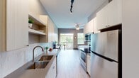 This single-floor studio is thoughtfully designed to maximize functionality within a compact footprint. The open-concept layout integrates the kitchen and living/sleeping area seamlessly, creating a cohesive and efficient living space. Light wood-style flooring runs throughout, lending a clean, contemporary feel.

The galley-style kitchen is well-appointed with stainless steel appliances, including a refrigerator, range, and built-in microwave. White cabinetry extends floor to ceiling on both sides, providing ample storage, while a subway tile backsplash and a double stainless steel sink with modern faucet add polished detail. Track lighting and flush-mount drum fixtures illuminate the kitchen corridor effectively.

The main living and sleeping area benefits from generous natural light through large windows and a sliding glass door that opens to a private balcony overlooking lush greenery. A ceiling fan enhances comfort and airflow. The walk-in closet off the sleeping area offers organized shelving and hanging space.

The bathroom features large-format tile wainscoting in warm earth tones, a white vanity with quartz-style countertop, a sizable mirror, and a shower-tub combination. The overall ambiance throughout the space is modern, clean, and efficiently designed.