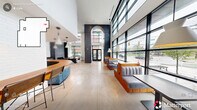 Located at 502 E Main Street in the heart of Durham, NC, this café offers a thoughtfully designed single-floor space that masterfully blends contemporary and industrial aesthetics. The interior is defined by dramatically high ceilings that amplify the sense of openness, drawing the eye upward and creating an airy, welcoming atmosphere throughout.

Floor-to-ceiling steel-framed windows line the exterior walls, flooding the space with abundant natural light and offering unobstructed views of the surrounding streetscape. The polished concrete tile flooring anchors the room with a clean, neutral foundation that complements the bold design elements above.

A striking dark accent wall with an arched architectural detail frames the main entrance, creating a dramatic focal point upon arrival. The seating area features custom wood-framed booths upholstered in soft grey, arranged to maximize both comfort and views. A distinctive live-edge communal table serves as a centerpiece near the service counter, adding warmth and a natural touch to the modern palette.

The service bar is finished with a rich wood countertop and accented by a teal ribbed panel, with a trio of modern pendant lights overhead. A built-in fireplace clad in dark concrete paneling adds a refined, lounge-like quality to the space. The overall ambiance is polished yet inviting, ideal for both casual gatherings and focused work.