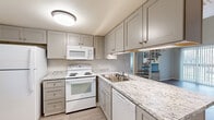 This two-story home in Lakewood, Colorado offers a well-designed layout across two floors, providing comfortable living with two bedrooms, two full bathrooms, and three closets. The main level features a thoughtfully updated kitchen appointed with granite-look countertops, gray shaker-style cabinetry, light wood-tone flooring, and a full suite of white appliances including a refrigerator, range, over-the-range microwave, and dishwasher. The kitchen opens toward the living area, which is highlighted by a cozy fireplace and soaring vaulted ceilings that lend an open, airy feel to the space. A striking staircase connects the two floors. The generously sized primary bedroom occupies a notable portion of the upper level, featuring carpeted flooring, a window with natural light, and angled ceiling lines that add architectural character. The second bedroom on the main level offers light wood-tone flooring and a reach-in closet. Both bathrooms are finished consistently with granite-look vanity countertops, white shaker cabinetry, tub-shower combinations, and black hardware accents. The clean, neutral palette and updated finishes throughout create a bright, cohesive ambiance well-suited to modern living in the Lakewood community.