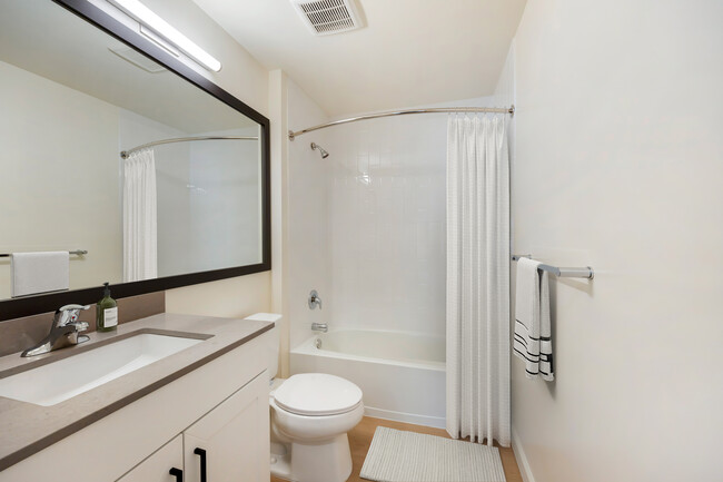 Baño de apartamentos nuevos con encimera de cuarzo gris, gabinetes blancos y pisos de superficie dura. - Avalon Commons