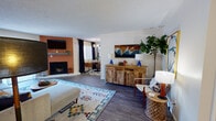 This well-appointed single-floor residence showcases a thoughtfully designed layout that balances comfort and style throughout. The open-concept living area is a standout, featuring a fireplace set against a rich terracotta accent wall, dark hardwood-style flooring, and a large sliding glass door that fills the space with natural light and leads to a private outdoor patio. Bold, earthy wall colors — deep rust and warm burgundy — complement the eclectic décor, creating a vibrant yet cohesive atmosphere.

The dining area is positioned adjacent to the living room and benefits from a large window overlooking greenery, creating a bright and inviting setting for meals. The kitchen offers ample cabinetry with a clean white finish, granite-style countertops, a double sink, and a dishwasher, with light wood-look flooring adding warmth to the functional space.

The residence includes two well-sized bedrooms, each featuring hardwood-style flooring, textured walls, and room for a workspace. One bedroom includes a window with natural light exposure, while both offer comfortable proportions. The bathroom is finished with a granite-topped vanity, large mirror, and clean neutral tones throughout. The overall ambiance of this space is warm, modern, and richly detailed.