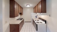 This single-floor residential unit offers a practical and comfortable layout across a well-organized floor plan. The open living and dining area features a combination of plush carpet and hardwood-style flooring, creating a welcoming atmosphere. A large sliding glass door floods the living space with natural light and provides access to a balcony or patio, offering views of lush greenery. A wall-mounted air conditioning unit and baseboard heating ensure year-round climate comfort.

The galley-style kitchen is efficiently designed with rich dark wood cabinetry lining both walls, offering generous storage space. White tile flooring, a double-basin sink, and a white electric range with a refrigerator complete the functional cooking space.

Two well-proportioned bedrooms are finished with soft carpeting, textured ceilings, and ceiling light fixtures. Each bedroom features windows that bring in natural light and views of surrounding greenery, along with baseboard heating for added comfort.

The bathroom is appointed with white tile flooring in a classic basketweave pattern, a vanity with storage, a toilet, and a full tub-shower combination. Throughout the unit, neutral tones and clean lines create a consistent, understated aesthetic that is both functional and easy to personalize.