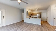 This 1-bedroom, 1-bathroom unit offers a thoughtfully designed open-concept floor plan that maximizes its functional living space. The living area features light-toned wood-style flooring, neutral gray walls, and a ceiling fan with built-in lighting, creating a bright and airy atmosphere. A large window allows natural light to fill the room, while a glass-paneled entry door adds an additional touch of openness.

The kitchen is a standout feature, anchored by a peninsula with a granite-style countertop and bar seating. Warm-toned cabinetry with modern hardware pairs with a classic subway tile backsplash, and geometric pendant lights hang above the peninsula for stylish task lighting. Stainless steel appliances — including a refrigerator, microwave, and range — complete the space.

The bedroom is carpeted for comfort, features a ceiling fan, and includes a window with blinds for natural light and privacy. An adjacent walk-in closet provides built-in shelving and hanging rods for ample storage.

The bathroom is clean and functional, offering a full tub/shower combo with built-in shelving, a granite-topped vanity, and wood-style flooring that ties in with the rest of the unit's design aesthetic.