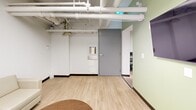 Located at 66 Spadina Rd in Toronto's Annex neighbourhood, this fitness facility offers a practical and well-appointed space across a single floor. The layout is divided into two primary areas: a dedicated exercise room and a lounge or relaxation room.

The exercise room is the centrepiece of the facility, featuring an exposed ceiling with white-painted pipes and ductwork that lend an industrial character to the space. The room is equipped with multiple treadmills, an elliptical trainer, a stationary bike, a weight bench, and a dumbbell rack. Two flat-screen televisions are mounted against a striking brick-print feature wall bearing the motivational phrase "Break Your Limits," adding energy and personality to the workout environment. Wall-mounted air conditioning units ensure a comfortable climate. Durable flooring throughout the exercise area is suited to high-traffic use.

Adjacent to the gym is a lounge area finished with light wood-look flooring and soft sage-green accent walls. This room features a large wraparound cream-coloured sectional sofa, a swivel accent chair, and a round coffee table, creating a calm and inviting space for rest or socializing. Recessed ceiling details and linear lighting contribute to a clean, modern aesthetic. A water station and washroom access are conveniently located nearby, rounding out the practical amenities of this well-organized fitness facility.
