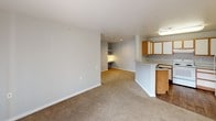 This single-floor, 2-bedroom, 2-bathroom residence features a practical and comfortable layout designed for everyday living. The open living area is finished with neutral-toned carpet and light gray walls, creating a clean, versatile backdrop. A sliding glass door allows natural light to fill the space and provides outdoor views. The living area connects seamlessly to the kitchen, which is set apart by a peninsula counter. The kitchen is outfitted with warm wood-toned cabinetry featuring white panel inserts, light-colored countertops, a double sink, and white appliances including a coil-top range and refrigerator. Wood-style flooring and a flush ceiling light fixture give the kitchen a practical, tidy feel. Both bedrooms are carpeted and finished with neutral walls. One bedroom includes a window with vertical blinds that brings in natural light, along with a closet. The two bathrooms each feature a tub-shower combination, a wood-vanity with a single sink, light countertops, and tile flooring. One bathroom includes a lighted vanity mirror, adding a bright, functional touch. The overall aesthetic throughout the residence is clean and understated, offering a move-in-ready environment with consistent finishes across all rooms.