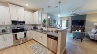 This contemporary 1120 square foot apartment offers a thoughtfully designed living space with two bedrooms and two bathrooms. The open-concept main area combines the living room, dining area, and kitchen, creating a seamless flow for everyday living and entertaining. The living room features a stylish accent wall, comfortable seating, and a large TV, while the adjacent dining area accommodates a modern glass-top table.

The kitchen is a highlight, boasting crisp white cabinetry, stainless steel appliances, and a subway tile backsplash. It's equipped with ample counter space and storage, including an oversized refrigerator. The primary bedroom, measuring 170 square feet, is spacious and bright, with large windows, a ceiling fan, and an en-suite bathroom. The second bedroom has been converted into a functional home office, featuring a sleek desk and vibrant wall art.

Both bathrooms showcase modern vanities, large mirrors, and contemporary fixtures. The apartment's neutral color palette is accented with pops of blue throughout, creating a cohesive and inviting atmosphere. Hardwood-style flooring in the main living areas and plush carpeting in the bedrooms add warmth and comfort. Ceiling fans in the bedrooms and living area ensure good air circulation. The unit also includes closet space with wire shelving for organization. Overall, this apartment combines style and functionality in a compact yet well-utilized floor plan.