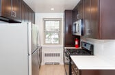 Located at 2 Hamilton Rd in Morristown, NJ, this single-floor residence combines classic architectural details with modern updates throughout its well-defined layout. Parquet hardwood flooring is a defining characteristic of the space, appearing consistently across the living areas and bedroom, adding warmth and visual texture to each room.

The expansive living area is bright and open, benefiting from natural light through a window that frames views of surrounding greenery. A wall-unit air conditioner and baseboard heating provide year-round climate control. The space flows seamlessly toward the entry, which features clean white-paneled doors and ample room for furniture arrangement.

The bedroom is generously sized, continuing the parquet flooring and offering access to a closet, providing practical storage. The kitchen has been thoughtfully updated with dark cabinetry extending to the ceiling, stainless steel appliances including a refrigerator, gas range, and microwave, white countertops, and subway tile backsplash. A window above the counter brings in natural light.

The bathroom is finished with white subway tile wainscoting, marble-look countertops, a white vanity with brushed gold hardware, tile flooring, and a tub-shower combination enclosed by sliding glass doors — presenting a clean, updated aesthetic throughout.