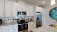 This thoughtfully designed single-floor residence offers a cohesive blend of modern finishes and functional living spaces. The kitchen is a standout feature, showcasing crisp white shaker cabinetry extending to the ceiling, granite countertops, a classic white subway tile backsplash, and a full suite of stainless steel appliances including a range with microwave above and a French door refrigerator. Wood-look flooring anchors the kitchen and flows seamlessly into the living area, where large sliding glass doors with vertical blinds invite natural light and provide access to the outdoors. The living space is open and comfortable, with a ceiling fan adding to the relaxed ambiance. The primary bedroom is generously sized, featuring plush carpeting, a ceiling fan, a large window, and a walk-in closet with built-in wire shelving. Its en-suite bathroom offers a granite-topped white vanity, tile flooring, and a glass-enclosed walk-in shower. A second bedroom provides a closet with double doors and soft carpeting. The second bathroom mirrors the home's refined aesthetic with a granite vanity, tile flooring, and a soaking tub with tiled surround. Every detail reflects a clean, contemporary design that balances style with everyday comfort.