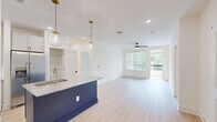 Located at 455 51st St in Wilmington, NC, this thoughtfully designed 2-bedroom, 2-bathroom residence offers a bright and modern living experience across a single, well-appointed floor. The open-concept kitchen and living area serves as the heart of the home, highlighted by a bold navy blue kitchen island topped with granite countertops and illuminated by globe pendant lights with gold-tone fixtures. White shaker cabinetry, a subway tile backsplash, and stainless steel appliances — including a refrigerator, range, microwave, and dishwasher — complete the kitchen. Light wood-look flooring flows throughout the main living areas, complementing the clean white walls and creating a fresh, airy ambiance. The living room benefits from abundant natural light through large windows and offers direct access to a private balcony. An in-unit washer and dryer add everyday convenience. Both bathrooms feature granite vanity countertops, white cabinetry, and matte black hardware accents. The primary bathroom includes a walk-in closet, while the secondary bath offers a full tub-shower combination. The bedrooms are carpeted for comfort and bathed in natural light. Two dedicated closets provide ample storage throughout the home.