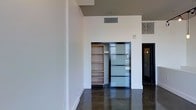This two-floor space showcases a clean, modern aesthetic rooted in contemporary industrial design. The polished concrete floors anchor the interior with a sleek, durable finish that reflects light and adds a sophisticated edge throughout. Soaring ceilings amplify the sense of openness, creating an airy, expansive atmosphere that flows naturally between areas.

A standout architectural detail is the frosted glass sliding door with a dark metal frame, which serves both as a functional partition and a design focal point. The frosted panels allow diffused natural light to pass through while maintaining privacy — a thoughtful balance of form and function. Adjacent to the sliding door, a built-in open shelving unit offers practical storage while contributing to the space's clean, organized look.

The walls are finished in a crisp white, providing a neutral backdrop that enhances the brightness of the interior and complements the darker tones of the flooring and door frames. Ceiling-mounted HVAC vents are seamlessly integrated into the design, maintaining the space's streamlined appearance. The two-floor layout provides distinct zones, offering both versatility and functionality. Overall, the space delivers a refined, minimalist environment well-suited for a variety of uses.
