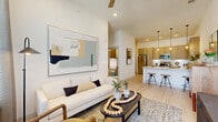 This thoughtfully designed one-bedroom, one-bathroom residence offers a modern open-concept layout that maximizes every square foot. Light wood-toned flooring flows throughout the main living areas, complementing the crisp white walls and elevated ceilings that lend an airy, spacious feel. The living room is a bright, welcoming space anchored by a ceiling fan and recessed lighting, with ample room for comfortable seating arrangements. It opens seamlessly to a well-appointed kitchen featuring flat-front wood cabinetry, a white quartz waterfall island with bar seating for three, stainless steel appliances, under-cabinet lighting, and pendant lights overhead — ideal for both everyday cooking and entertaining. The bedroom is a serene retreat with plush carpeting, large windows that invite natural light, and access to a closet. The full bathroom includes a tiled tub-shower combination, wood-accented cabinetry, and light wood flooring that ties the space together. Additional features include a dedicated hallway, a utility room, in-unit laundry, and a private patio. The overall ambiance is clean, contemporary, and functional, making this a well-rounded residence suited for modern living.