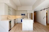 Located on the 10th floor at 1425 New York Ave NW in the heart of Washington, DC, this thoughtfully designed two-bedroom, two-bathroom residence offers a clean, contemporary aesthetic throughout. Light oak hardwood flooring flows seamlessly across the open-concept living space, complemented by crisp white walls and recessed lighting that create a bright, airy atmosphere.

The kitchen is a standout feature, boasting floor-to-ceiling white flat-panel cabinetry, a striking marble-veined quartz center island, a quartz backsplash, and a full suite of stainless steel appliances including a built-in wine cooler. A stylish barn door adds a modern industrial touch to the living area.

The hallway is distinguished by a bold steel-framed glass partition, lending an architectural flair while maintaining an open feel. Both bedrooms are well-proportioned, featuring light wood flooring and ample closet space, including double-door closets. The primary bathroom offers a sleek walk-in shower with frameless sliding glass doors, a wide vanity with brushed gold fixtures, and large-format stone tile flooring. The second bathroom features a full soaking tub and matching stone tile. An in-unit laundry area adds everyday convenience to this polished urban residence.