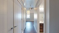 This thoughtfully designed single-floor space offers an efficient and modern layout that maximizes every square foot. The open-concept kitchen is a standout feature, boasting rich dark-stained wood cabinetry that extends to impressive heights, a full suite of stainless steel appliances including a refrigerator, electric range, built-in microwave, and dishwasher, complemented by a clean white subway tile backsplash and light countertops. The main living area impresses with soaring ceilings, dual-tone blue-grey and white walls, and a ceiling fan that enhances the airy atmosphere. Multiple windows fitted with roller shades invite generous natural light while maintaining privacy, and dark hardwood-style flooring flows cohesively throughout. A well-appointed hallway leads to the bathroom, which features large-format tile flooring, a dark wood vanity with a white countertop, a glass-enclosed shower/tub combination with white tile surround, and direct access to a dedicated walk-in closet equipped with built-in wire shelving and hanging rods. The overall ambiance is clean, modern, and functional, reflecting a well-considered use of space with quality finishes throughout.