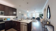 This single-story residence offers a thoughtfully designed open-concept layout that seamlessly connects the kitchen, dining, and living areas. The kitchen is outfitted with rich dark cabinetry, a full suite of stainless steel appliances—including a refrigerator, range, microwave, and dishwasher—and a peninsula with a white countertop that doubles as a casual dining or prep space. Stylish pendant lighting illuminates the peninsula, while crown molding adds a refined touch throughout the common areas. Wood-style flooring flows across the main living space, which benefits from large windows that invite generous natural light and a ceiling fan overhead.

The living area provides a comfortable, open atmosphere with ample room for seating and entertaining. Two bedrooms feature plush carpet, natural light from well-positioned windows, and neutral tones. The primary bedroom connects to a generously sized walk-in closet with wire shelving systems. Both bathrooms include dark vanity cabinetry with white countertops and wood-style flooring. A dedicated laundry area houses a full-size top-loading washer and dryer with overhead wire shelving for added storage convenience.