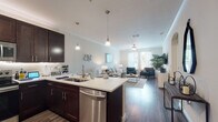 This single-story residence offers a thoughtfully designed open-concept layout that seamlessly connects the kitchen, dining, and living areas. The kitchen is outfitted with rich dark cabinetry, a full suite of stainless steel appliances—including a refrigerator, range, microwave, and dishwasher—and a peninsula with a white countertop that doubles as a casual dining or prep space. Stylish pendant lighting illuminates the peninsula, while crown molding adds a refined touch throughout the common areas. Wood-style flooring flows across the main living space, which benefits from large windows that invite generous natural light and a ceiling fan overhead.

The living area provides a comfortable, open atmosphere with ample room for seating and entertaining. Two bedrooms feature plush carpet, natural light from well-positioned windows, and neutral tones. The primary bedroom connects to a generously sized walk-in closet with wire shelving systems. Both bathrooms include dark vanity cabinetry with white countertops and wood-style flooring. A dedicated laundry area houses a full-size top-loading washer and dryer with overhead wire shelving for added storage convenience.