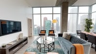 This contemporary high-rise residence offers an impressive blend of modern design and urban living. The open-concept living area is defined by dramatic floor-to-ceiling windows that stretch the full height of the space, flooding the interior with natural light and framing sweeping panoramic views of the downtown city skyline. Exposed concrete columns add an industrial character that complements the clean, modern aesthetic throughout.

The kitchen is outfitted with high-end stainless steel appliances, including a gas range, built-in microwave, dishwasher, and a french-door refrigerator. Dark wood-grain lower cabinetry is paired with glossy white upper cabinets and crisp white countertops, creating a refined, contemporary look.

Both bedrooms are generously proportioned, each benefiting from floor-to-ceiling windows that capture city views and fill the rooms with natural light. Light wood flooring and neutral tones carry through the space, reinforcing a cohesive and calming palette.

The residence includes two full bathrooms. The primary bathroom features a glass-enclosed walk-in shower, a dual-sink vanity with dark cabinetry and white countertops, and recessed lighting. The secondary bathroom offers a tub-shower combination with equally clean, modern finishes. Together, these spaces deliver a polished, functional urban living experience.