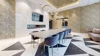 Located at 202 Burnhamthorpe Rd E in Mississauga, Ontario, this elegantly appointed space showcases an exceptional level of interior design craftsmanship. The layout encompasses a living area, a generously sized primary room, and an additional unclassified space, all unified by a cohesive luxury aesthetic.

The centerpiece of the space is a dramatic conference-style dining area featuring a long, sleek table surrounded by plush, quilted velvet chairs with gold-toned legs. Overhead, an eye-catching sculptural chandelier of interlocking circular rings commands attention, while a gold-patterned coffered ceiling adds warmth and depth above.

The floors are a standout architectural feature — large-format marble tiles arranged in a bold geometric pattern of white, blue, and dark stone create a visually dynamic foundation throughout. One wall is clad in striking white veined marble and incorporates a sleek linear fireplace beneath a mounted television, lending both warmth and sophistication.

Bold, gold-toned geometric wallcoverings adorn multiple walls, complemented by warm wood cabinetry and paneling that add organic texture. The lounge area features a plush sofa positioned before tall, frosted windows that allow soft, diffused natural light to fill the room while maintaining privacy. The overall ambiance is refined, contemporary, and decidedly upscale.