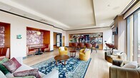Located at 570 North 5th Street in Philadelphia's Northern Liberties neighborhood, this generously scaled single-floor amenity space offers a sophisticated and eclectic environment designed for socializing and relaxation. Light wide-plank hardwood flooring runs throughout, unifying the various distinct zones seamlessly.

The lounge area anchors the space with layered seating arrangements, including plush sofas, vibrant yellow swivel chairs, and richly upholstered accent chairs arranged around decorative rugs and walnut coffee tables. Intimate booth-style nooks, framed by warm wood paneling and bold floral wallcoverings in deep burgundy tones, provide semi-private gathering spots. A fully equipped bar features leather counter seating, stone-clad detailing, and built-in shelving — ideal for entertaining.

A dedicated game room hosts a ping pong table beneath a sculptural circular chandelier, complemented by tufted leather banquette seating set against a geometric textured accent wall. A separate lounge zone showcases a floor-to-ceiling wood-clad fireplace wall flanked by floor-to-ceiling windows offering sweeping Philadelphia skyline views.

A bright transitional corridor with warm wood wall cladding and expansive glass doors opens directly onto an outdoor terrace, flooding the interior with natural light and providing seamless indoor-outdoor connectivity.
