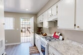Located at 19015 Kittridge St in the Reseda neighborhood of Los Angeles, CA, this one-bedroom, one-bathroom unit offers a practical and comfortable single-floor layout. The living room is bright and welcoming, featuring light gray hardwood-style flooring, a textured ceiling, and a large window with vertical blinds that allows generous natural light to filter in. A wall-mounted AC unit provides climate control, and the open sightline connects seamlessly to the rest of the unit via a hallway. The galley-style kitchen is well-appointed with white cabinetry extending to the ceiling, granite-look countertops, a gas range, a single-basin sink, and recessed lighting overhead. A door at the end of the kitchen opens directly to the exterior, enhancing ventilation and accessibility. The bedroom features plush carpeting, a textured ceiling, recessed lighting, and a large window with vertical blinds offering outdoor views and natural light. The bathroom is clean and efficiently designed, with a white vanity, a mirrored medicine cabinet, a full-size soaking tub with tiled surround, and hardwood-style flooring. Neutral warm-beige tones throughout the unit create a cohesive and inviting ambiance.
