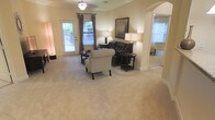 This single-floor residence offers a thoughtfully designed layout with an inviting and comfortable ambiance throughout. The living room serves as the centerpiece of the space, featuring warm neutral-toned wall-to-wall carpeting that adds a sense of coziness underfoot. Crown molding along the upper walls lends a classic, refined architectural detail to the room, while a ceiling fan with a light fixture provides both style and function overhead.

Natural light filters into the living area through a large window dressed with elegant floor-length curtain panels, offering views of lush greenery outside. A glass door further enhances the connection to the outdoors, brightening the space and providing access to an exterior area. The room is generously proportioned, accommodating a seating arrangement that includes a tufted leather sofa and a cushioned accent chair, creating a welcoming focal point.

A graceful arched doorway transitions seamlessly into an adjacent room, adding architectural charm and an open, airy feel to the overall layout. The soft, neutral color palette throughout the living area contributes to a calm and versatile atmosphere, making the space well-suited for both relaxing and entertaining.