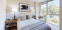 This contemporary single-floor residence is thoughtfully designed with a clean, modern aesthetic and an emphasis on natural light throughout. The open-concept living area is anchored by dramatic floor-to-ceiling windows that frame sweeping views of the city skyline and lush treetops, flooding the space with daylight and creating a seamless connection to the urban landscape beyond. Rich hardwood flooring flows through the main living areas, adding warmth to the sleek interior.

The kitchen is a standout feature, offering white shaker cabinetry, dark granite countertops, and a full suite of stainless steel appliances including a refrigerator, electric range, and built-in microwave. A peninsula with an overhang accommodates contemporary bar stools, making it an ideal spot for casual dining or entertaining.

The residence includes two well-appointed bedrooms. The primary bedroom benefits from generous natural light through large windows overlooking greenery, complemented by soft neutral tones and plush carpeting. The second bedroom maintains a similarly calm, understated character.

Two bathrooms complete the layout. One features a glass-enclosed walk-in shower, dark granite vanity, and white cabinetry, while the second offers a clean, tile-floored design with a well-lit vanity and ample storage. Together, these spaces deliver a polished, functional living environment with a refined modern sensibility.