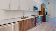 Located at 730 16th Street in Sacramento, CA, this studio unit at The Mansion offers a well-designed, single-floor open layout that maximizes functionality and style. Light wood-tone vinyl flooring runs throughout the entire space, providing a clean, cohesive aesthetic.

The living area benefits from a striking floor-to-ceiling window with transom, flooding the room with natural light and offering views of the tree-lined street outside. The soaring ceiling height enhances the sense of openness throughout.

The kitchen is thoughtfully appointed with a two-tone cabinet design — warm wood lower cabinets paired with crisp white upper cabinets — complemented by a white subway tile backsplash and light quartz countertops. A full suite of stainless steel appliances includes a refrigerator, electric range, over-the-range microwave, and dishwasher, along with a single-basin sink with a modern pull-down faucet.

The bathroom features light wood-tone flooring consistent with the rest of the unit, a wood-toned vanity with a white countertop, and a full tub-shower combination with elegant marble-style wall surround and a curved shower rod. The bright white walls throughout the unit contribute to a fresh, contemporary ambiance ideal for urban living.