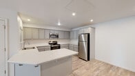 This single-floor space offers a clean, contemporary design throughout. The kitchen serves as a central highlight, featuring gray shaker-style cabinetry, bright white countertops, and a full suite of stainless steel appliances including a refrigerator, range, microwave, and dishwasher. A peninsula provides additional counter space and casual seating potential. Light wood-style flooring runs through the kitchen and living areas, contributing to a bright, cohesive aesthetic complemented by recessed lighting overhead.

The bedrooms are finished with neutral wall-to-wall carpet and ceiling fans, creating a comfortable atmosphere. Each bedroom includes a window allowing natural light and outdoor views, along with closet storage. One bedroom features a walk-in closet with built-in shelving.

The bathrooms maintain the space's consistent modern palette, with light wood-style flooring, white vanities with light countertops, and sliding glass shower/tub enclosures with brushed nickel hardware. One bathroom includes a small window for added ventilation and natural light.

Overall, the space presents a well-maintained, move-in-ready environment with a neutral color scheme that provides a versatile backdrop throughout.