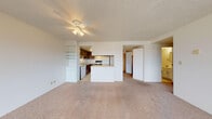 Located at 1080 Patterson St in Eugene, Oregon, this single-floor residence offers a clean, functional layout with a bright and open feel throughout. The spacious living area is lined with large, floor-to-ceiling windows along one wall, flooding the space with natural light and framing elevated views of the Eugene cityscape and surrounding greenery. Soft wall-to-wall carpeting, white textured walls, and a textured ceiling with a ceiling fan contribute to a simple, neutral aesthetic throughout the living and bedroom spaces.

The kitchen is thoughtfully integrated into the open floor plan, featuring dark wood cabinetry, a central peninsula with a light countertop, a white refrigerator, an electric range, a dishwasher, and a sink. Tile flooring in the kitchen transitions seamlessly to the carpeted living area. Built-in open shelving near the kitchen provides additional storage and display space.

The bedroom offers a quiet, carpeted retreat with ample wall space and access to a closet. The full bathroom includes a tiled tub-shower combo, a single vanity with under-sink storage, and mosaic tile flooring, maintaining the unit's clean and functional character. A hallway connects the main living spaces efficiently, completing this well-organized Eugene residence.