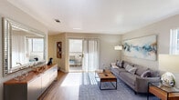 This well-designed single-floor residence offers a thoughtfully laid-out interior with a warm, contemporary aesthetic. The living room serves as the heart of the home, featuring wood-look flooring, large windows, and sliding glass doors that open to a private outdoor patio, flooding the space with abundant natural light. A large decorative mirror and a low-profile credenza add functional style to the living area.

The kitchen is efficiently designed with white cabinetry, granite-style countertops, and stainless steel appliances, including a range and over-the-range microwave. Wood-look flooring continues throughout, tying the spaces together cohesively.

Adjacent to the living area, the dining space accommodates a round wood table beneath a ceiling fan, with a window overlooking greenery outside — ideal for casual meals in a relaxed setting.

The bedroom is a comfortable retreat, offering a closet, wood-look flooring, and ample wall space. The bathroom features a tub-shower combination with a curved curtain rod, granite-style vanity countertop, white cabinetry, and wood-look flooring, maintaining the clean and consistent design language found throughout the home.

Overall, the residence presents a light, neutral palette with warm wood tones that create an inviting and functional living environment.