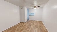 This well-organized 2-bedroom, 2-bathroom single-floor residence makes thoughtful use of its compact footprint. The combined kitchen and living area serves as the heart of the home, featuring warm wood-look laminate flooring, a textured ceiling, and a ceiling fan with integrated lighting. A pass-through window connects the kitchen to the living space, enhancing the open feel. The kitchen is equipped with white cabinetry, a full-size refrigerator, an electric range with overhead ventilation, a sink, and tile flooring in a neutral stone pattern, along with a dedicated pantry for additional storage.

The primary bedroom offers comfortable proportions, plush carpeting, a ceiling fan, a window with natural light, and direct access to a walk-in closet outfitted with built-in shelving. The second bedroom also features carpeting and a ceiling fan. Both bathrooms include tiled tub-and-shower surrounds — one with warm earth-toned tile and another with lighter neutral tiling — and tile flooring throughout.

Additional functional spaces include a hallway connecting the main areas, three closets total providing ample storage, and a utility room. The consistent white walls and clean finishes throughout lend the space a bright, cohesive aesthetic.