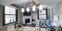 Located at 526 Superior Avenue in the heart of Cleveland, Ohio, this single-floor residence combines urban sophistication with thoughtful design. The open-concept layout seamlessly connects the kitchen and living area, creating a welcoming and functional space filled with natural light from large, dark-framed windows that frame dynamic city views.

The kitchen is a standout feature, appointed with dark espresso cabinetry, granite countertops, stainless steel appliances, and a central island with a deep single-basin sink and pendant lighting overhead. Rich hardwood flooring runs throughout, anchoring the space with warmth and continuity.

The living area is centered around a classic white fireplace with a mounted television above, flanked by expansive windows on two sides. A ceiling fan adds comfort to the generously proportioned room, which offers ample space for a full seating arrangement.

The bedroom, visible in the floor plan, is well-proportioned and also benefits from natural light and a ceiling fan. Additional spaces include a bathroom and storage areas. Throughout the residence, the interplay of dark wood tones, granite surfaces, and neutral walls creates a polished, contemporary aesthetic well-suited to downtown Cleveland living.