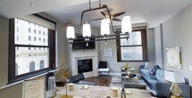 Located at 526 Superior Avenue in the heart of Cleveland, Ohio, this single-floor residence combines urban sophistication with thoughtful design. The open-concept layout seamlessly connects the kitchen and living area, creating a welcoming and functional space filled with natural light from large, dark-framed windows that frame dynamic city views.

The kitchen is a standout feature, appointed with dark espresso cabinetry, granite countertops, stainless steel appliances, and a central island with a deep single-basin sink and pendant lighting overhead. Rich hardwood flooring runs throughout, anchoring the space with warmth and continuity.

The living area is centered around a classic white fireplace with a mounted television above, flanked by expansive windows on two sides. A ceiling fan adds comfort to the generously proportioned room, which offers ample space for a full seating arrangement.

The bedroom, visible in the floor plan, is well-proportioned and also benefits from natural light and a ceiling fan. Additional spaces include a bathroom and storage areas. Throughout the residence, the interplay of dark wood tones, granite surfaces, and neutral walls creates a polished, contemporary aesthetic well-suited to downtown Cleveland living.