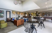 Located in Atlanta, GA (30316), this single-floor community amenity space offers a well-rounded mix of social, recreational, and functional areas designed for modern living. The open-plan layout is anchored by light-toned large-format tile flooring that flows seamlessly throughout, lending a clean and cohesive aesthetic.

The central gathering area features a lounge with a bold navy accent wall, wall-mounted flat-screen TV, built-in bench seating, and a rich leather sofa paired with eclectic accent pieces, creating an inviting and relaxed atmosphere. Adjacent to the lounge, a game room provides a full-sized pool table and bistro-style seating near floor-to-ceiling glass doors that open onto a balcony overlooking lush tree canopy views.

The kitchen and dining zone includes a sleek island with a striking green tile base, stainless steel hood vent, and bar stool seating, complemented by an extensive gallery wall of framed artwork that adds character to the space. Nearby, a dedicated co-working area offers built-in white desks and partition shelving with colorful red and neutral panel accents, providing semi-private workstations ideal for focused tasks. Restroom facilities are also accessible within the space. Together, these areas create a dynamic, multi-purpose environment suited for socializing, working, and recreation.