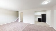 This two-floor residence at 1699 Shanley Dr in Columbus, Ohio offers a clean, contemporary layout with thoughtful updates throughout. The main level features a spacious carpeted living area that flows openly toward the kitchen, which has been outfitted with crisp white shaker-style cabinetry, marble-look countertops, light wood-style flooring, and black and stainless steel appliances including a range, dishwasher, microwave, and refrigerator. A staircase connects both levels, and a separate entry door is accessible from the main living space. The bedrooms are generously sized with soft carpeting, neutral toned walls, and windows that allow natural light to filter in. Wall-unit air conditioning and baseboard heating are present in the bedroom areas, ensuring year-round comfort. The bathrooms reflect a refreshed aesthetic — the upper-level bath features vaulted ceilings, light wood-style flooring, a white vanity with brushed gold hardware, and a framed mirror, while the lower-level bath includes a full tub and shower combination with brushed nickel fixtures. Overall, the space presents a neutral, move-in-ready environment with modern finishes balanced against a practical, functional layout.