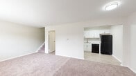 This two-floor residence at 1699 Shanley Dr in Columbus, Ohio offers a clean, contemporary layout with thoughtful updates throughout. The main level features a spacious carpeted living area that flows openly toward the kitchen, which has been outfitted with crisp white shaker-style cabinetry, marble-look countertops, light wood-style flooring, and black and stainless steel appliances including a range, dishwasher, microwave, and refrigerator. A staircase connects both levels, and a separate entry door is accessible from the main living space. The bedrooms are generously sized with soft carpeting, neutral toned walls, and windows that allow natural light to filter in. Wall-unit air conditioning and baseboard heating are present in the bedroom areas, ensuring year-round comfort. The bathrooms reflect a refreshed aesthetic — the upper-level bath features vaulted ceilings, light wood-style flooring, a white vanity with brushed gold hardware, and a framed mirror, while the lower-level bath includes a full tub and shower combination with brushed nickel fixtures. Overall, the space presents a neutral, move-in-ready environment with modern finishes balanced against a practical, functional layout.