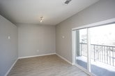 This single-floor unit presents a thoughtfully designed layout with a cohesive modern aesthetic throughout. The open-concept kitchen and living area form the heart of the space, finished with light wood-tone flooring that contrasts cleanly against neutral gray walls and crisp white baseboards. The kitchen is well-equipped with a full suite of stainless steel appliances, including a French door refrigerator, electric range, over-the-range microwave, and dishwasher. Dark espresso-toned cabinetry extends to the ceiling, complemented by open shelving, white subway tile backsplash, and light quartz countertops. A utility closet with built-in wire shelving is accessible just off the kitchen corridor, alongside an electrical panel conveniently housed in the wall. The bedroom offers a calm, functional space with the same warm flooring, gray walls, and a sliding-door closet. The bathroom features a dark wood vanity with drawers and cabinet storage beneath a white quartz countertop, an undermount sink, brushed nickel fixtures, and a large framed mirror with overhead lighting. The consistent material palette and clean finishes give the unit a polished, contemporary character throughout.