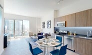 Located on the 19th floor in Miami's vibrant Edgewater neighborhood, this one-bedroom, one-bathroom residence offers a well-designed open-concept layout with modern finishes throughout. Light wood-look tile flooring flows seamlessly across the entire unit, complementing the clean, white walls and soaring ceilings that enhance the sense of space.

The combined kitchen and living area serves as the heart of the home. The kitchen features warm wood-grain cabinetry extending to ceiling height, stainless steel appliances including a range, microwave, and refrigerator, dark countertops, and under-cabinet LED accent lighting. A glass-top dining table with bold teal chairs provides an elegant dining space adjacent to the kitchen.

The living area is bathed in natural light through floor-to-ceiling sliding glass doors that open onto the balcony, offering sweeping views of the Miami skyline. The bedroom continues the bright, airy aesthetic with its own floor-to-ceiling window framing city views, soaring ceilings, and a sliding barn-style door. Three closets, including a well-appointed walk-in with built-in shelving and hanging systems, provide generous storage.

The bathroom features wood-grain vanity cabinetry, a backlit mirror, a tiled soaking tub and shower combination, and crisp white countertops. Additional conveniences include an in-unit laundry and a utility room.