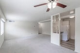 This single-floor unit offers a functional and straightforward layout with a neutral color palette throughout. The living area is generously proportioned, finished with wall-to-wall carpet, and equipped with a ceiling fan and light fixture. Natural light enters through a large window, contributing to a bright and open feel. The space flows toward the kitchen, which is partially separated by a built-in open shelving divider. The kitchen features white cabinetry with brushed nickel hardware, dark laminate countertops, a stainless steel sink, and wood-look flooring. A white gas range and refrigerator are included appliances.

The bedroom is a well-sized, carpeted room with a large window offering exterior views and an abundance of built-in closet storage, including multiple sections with shelving and hanging rods. The bathroom is clean and functional, with white subway tile surrounding the bathtub and shower combination, a toilet, and a vanity with overhead cabinetry. Throughout the unit, the warm beige tones and neutral finishes create a simple, livable ambiance suited for a variety of occupants.