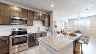 This single-floor residence is designed with a cohesive, modern aesthetic highlighted by light wood-style flooring and neutral tones throughout. The kitchen serves as a central feature, showcasing rich dark-brown cabinetry with sleek hardware, white subway tile backsplash, light granite countertops, and a full suite of stainless steel appliances including a refrigerator, range, microwave, and dishwasher. A central island with a granite surface provides additional prep and casual dining space. The kitchen opens seamlessly into the living area, which benefits from natural light streaming through large windows with outdoor views of greenery. A ceiling fan adds practical comfort to the living space. Bedrooms are bright and versatile, featuring the same light flooring, ceiling fans, and windows that invite natural light. The bathroom includes wood-style flooring, a vanity with granite countertop, dark cabinetry, a soaking tub with white subway tile surround, and access to a walk-in closet. Throughout the unit, clean lines, recessed lighting, and a consistent neutral palette create a polished, contemporary ambiance.