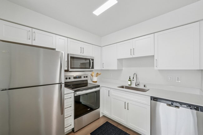 Renovated Package II kitchen with stainless steel appliances, updated white cabinetry, quartz countertops, and hard surface flooring - eaves Walnut Creek