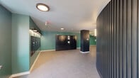 Located at 6515 Ridge Avenue in Philadelphia's Roxborough neighborhood, this thoughtfully designed building lobby and mail area offers a welcoming first impression with a distinctive modern aesthetic. The space is defined by bold teal-painted walls paired with crisp white ceilings and light-toned tile flooring, creating a bright, clean atmosphere throughout.

A standout architectural feature is the curved, dark slatted accent wall that anchors the main lobby area, adding visual depth and a refined, contemporary character. Flush circular light fixtures and wall-mounted sconces provide warm, even illumination across all areas, while large windows along the corridor allow natural light to filter in and offer views of the surrounding streetscape.

The mail and package area is well-equipped with a full bank of individual resident mailboxes and a modern smart parcel locker system, providing secure and convenient package retrieval. Elevator access is clearly positioned within the lobby, alongside additional doorways that connect to other areas of the building.

The generous corridor leads residents smoothly from the entrance through to the elevator lobby, maintaining a cohesive design language throughout. The overall ambiance is polished and functional, balancing bold design choices with practical amenities that serve the needs of a modern residential building.