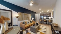 This thoughtfully designed single-floor residence offers a seamless blend of contemporary style and functional living. The open-concept living area serves as the heart of the home, anchored by a dramatic deep navy accent wall that provides a bold contrast to the crisp white ceilings and light hardwood-style flooring. Recessed lighting and a ceiling fan illuminate the space, which flows effortlessly into the kitchen and dining area. The kitchen is well-appointed with dark espresso cabinetry, stainless steel appliances including a refrigerator with ice maker, electric range, and microwave, along with a granite-topped island that doubles as a breakfast bar with bar seating. Two bedrooms offer distinct personalities — one features a moody, art-filled atmosphere with a gallery wall, pendant lighting, and a soft color palette, while the second is bright and airy with large windows dressed in floor-to-ceiling drapes. The bathroom is finished with vertically tiled tub surround, a granite vanity, dark wood cabinetry, and wood-look flooring. Throughout the residence, consistent design choices — including panel-style interior doors and a warm, curated color palette — create a cohesive and inviting ambiance.