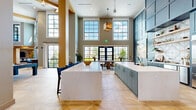 Located at 34 Ramsey Branch Rd, this expansive single-floor community space offers a generously sized, open-concept layout designed for both socializing and relaxation. The architecture is defined by soaring double-height ceilings, bold gold-toned structural beams, and floor-to-ceiling multi-pane windows that flood the interior with natural light and provide sweeping outdoor views.

The gourmet kitchen is a standout feature, showcasing slate-blue cabinetry that extends to the ceiling, a dramatic waterfall-edge marble island with bar seating, stainless steel appliances, and a patterned tile backsplash. A built-in banquette nook with warm leather upholstery and plaid accent chairs provides an intimate dining option.

The game area includes a full-size billiards table and additional game furnishings set beneath the towering windows, creating an energetic yet open atmosphere. A dedicated lounge zone features plush patterned sofas, a built-in bookshelf, and a cozy seating arrangement centered around a flat-screen TV set against a bold plaid accent wall.

Throughout, the herringbone-patterned light wood flooring ties each zone together seamlessly. The space transitions into a quieter living area with sectional seating, wall-mounted art, and warm accent lighting, offering a more intimate retreat within the larger layout.