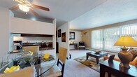 This single-floor residence at 26101 Country Club Blvd in North Olmsted, Ohio, offers a well-organized layout connecting living, dining, kitchen, and sleeping areas in a cohesive flow. The living room is a comfortable, carpeted space anchored by a large sliding glass door with vertical blinds that invite generous natural light and provide views of the surrounding outdoor area. A wall-mounted air conditioning unit and baseboard heating ensure year-round comfort. The dining area, positioned adjacent to the living room and kitchen pass-through, features a ceiling fan overhead and tile flooring at the entry transition. The galley-style kitchen is equipped with dark wood cabinetry, granite-look countertops, a full-size refrigerator, and an electric range with overhead ventilation. The primary bedroom is generously sized with plush carpeting, a walk-in closet, and direct access to an en-suite bathroom. The second bedroom also offers carpet, a standard closet with bi-fold doors, and a window with outdoor light. Two full bathrooms are present — one with a tub/shower combination and white tile flooring, the other with a vanity and mirrored medicine cabinet. The entryway features tile flooring, providing a clean transition into the carpeted main living spaces throughout this well-appointed home.