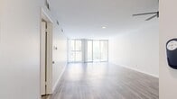 This well-appointed single-floor unit offers a thoughtfully designed open layout that seamlessly integrates the kitchen and living room into one cohesive, light-filled space. Light-toned hardwood flooring runs throughout, complementing the crisp white walls and clean lines that define the unit's modern aesthetic.

The living area is generously proportioned, bathed in natural light that streams through a wall of floor-to-ceiling sliding glass doors and windows. These open onto a private balcony, offering views of the surrounding cityscape and creating a seamless indoor-outdoor connection. Recessed lighting adds a polished touch to the bright, airy atmosphere.

The kitchen is well-equipped and stylishly finished, featuring white shaker-style cabinetry with brushed nickel hardware, neutral quartz countertops, and a full suite of stainless steel appliances including a gas range, over-the-range microwave, refrigerator, and dishwasher. The kitchen's open orientation toward the living space makes it ideal for entertaining. A dedicated closet provides practical storage within the unit. The overall ambiance is clean, contemporary, and welcoming, with a neutral palette throughout that offers a versatile canvas for personalization.