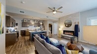This thoughtfully designed 2-bedroom, 2-bathroom single-floor residence offers a seamless open-concept layout that connects the living, dining, and kitchen areas into one cohesive, functional space. The living room is anchored by a sleek built-in electric fireplace set against a wood-paneled accent wall, complemented by a ceiling fan, large windows, and a glass door that floods the space with natural light. The well-equipped kitchen features dark espresso cabinetry, granite-style countertops, a herringbone tile backsplash, stainless steel appliances, and a central island with bar seating beneath stylish geometric pendant lights. Wide-plank wood-look flooring flows throughout the main living areas, adding warmth and continuity. Both bedrooms are carpeted and generously sized, with ceiling fans, large windows, and ample natural light. The primary bedroom is a comfortable retreat offering significant square footage. The two bathrooms are finished with dark wood vanities, granite countertops, and framed mirrors. A dedicated walk-in closet provides convenient storage. Two hallways connect the private areas of the home, completing a practical and polished floor plan throughout.