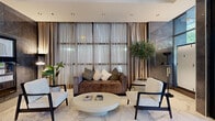 The lobby of Landis Residences is a thoughtfully designed entrance space that sets an elevated tone for the building. Floor-to-ceiling glass doors and expansive glazed panels at the entrance flood the interior with natural light while providing clear sightlines to the tree-lined street beyond, creating an open and connected atmosphere. Underfoot, large-format polished marble tiles in white and grey veining extend throughout the entire space, lending a sense of refinement and continuity. The seating area is appointed with a plush brown velvet sofa, a pair of cream boucle accent chairs with dark wood frames, and a sculptural oval coffee table—all arranged to create a comfortable and stylish gathering point. Lush indoor plants, including a statement olive tree and tropical foliage, bring warmth and life to the space. A dedicated reception area features a striking marble-fronted desk framed by floor-to-ceiling grey stone tile cladding and illuminated by elegant oval pendant lights. A modern directional chandelier provides additional ambient lighting overhead. The overall ambiance is contemporary and luxurious, balancing clean architectural lines with warm, curated furnishings to deliver a welcoming and impressive arrival experience.