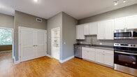 This 1-bedroom, 1-bathroom unit offers a thoughtfully designed single-floor layout that maximizes every square foot. Warm hardwood-style flooring and cool gray walls create a cohesive, modern aesthetic that flows throughout the entire space.

The kitchen is a standout feature, outfitted with crisp white shaker-style cabinetry extending to the ceiling for ample storage, dark gray countertops, and a full suite of stainless steel appliances including a range, microwave, refrigerator with ice and water dispenser, and dishwasher. A single-basin sink with a modern faucet completes the functional workspace, while track lighting overhead brightens the area effectively.

The bedroom is generously sized for the overall footprint of the unit, featuring tall ceilings that enhance the sense of space, large windows that invite natural light, and a louvered double closet offering practical storage.

The bathroom is finished with a clean, contemporary aesthetic, featuring a full tub and shower combination with tiled surround, a gray vanity with a white countertop, a large frameless mirror, and light marble-style tile flooring that adds a touch of elegance.

Throughout the unit, white trim and baseboards provide crisp contrast against the gray walls, lending the space a polished, move-in-ready feel.